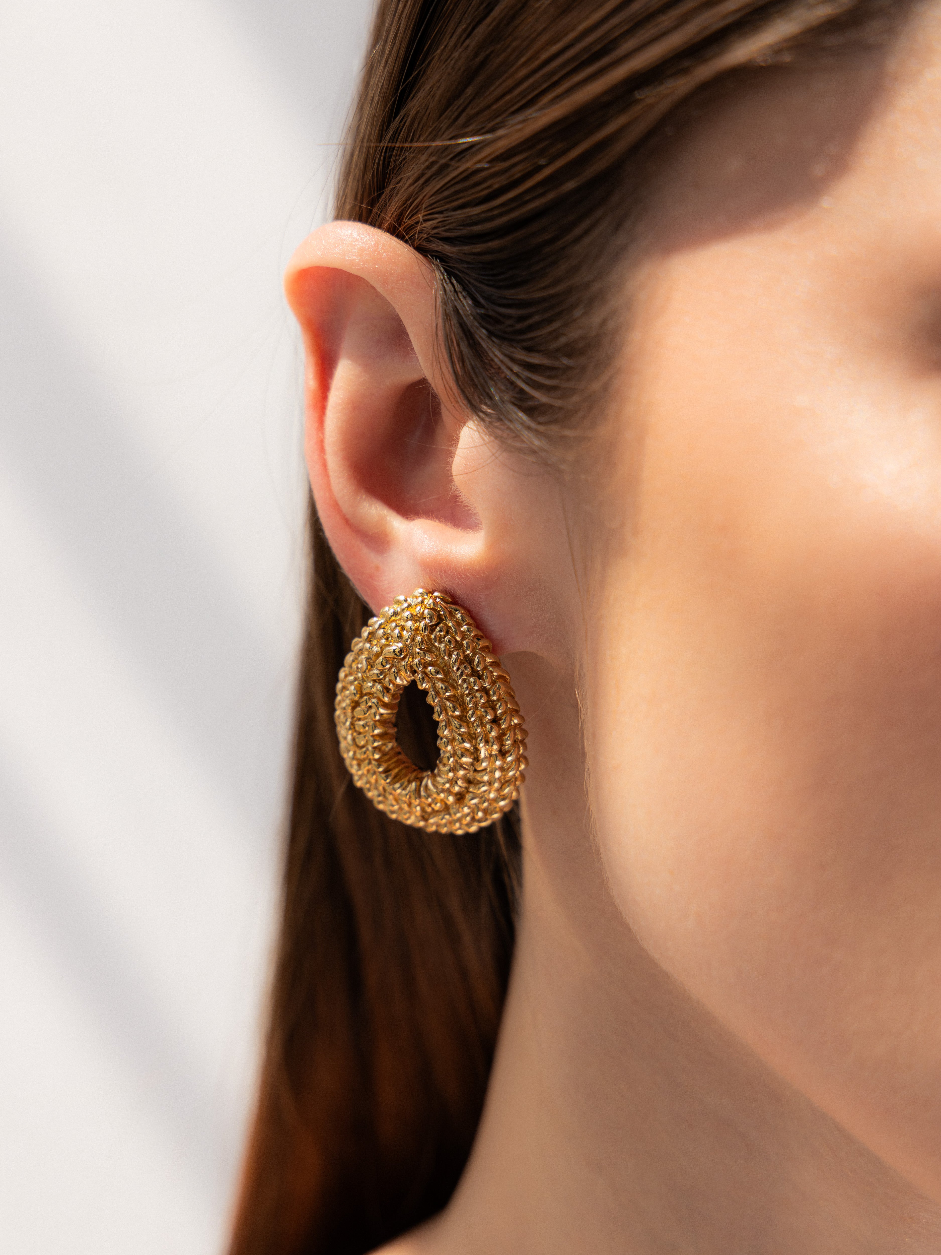 Gold hoop earring worn by a person with a neutral background